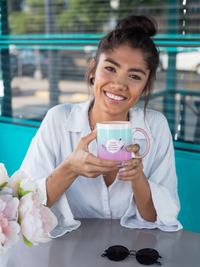 jeune femme souriante assise et tenant un Mug Éclat Astral Balance en céramique rose dans les mains